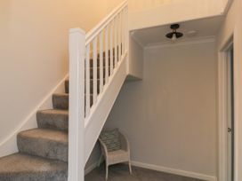 A staircase with carpet and a white railing next to a small corner with a wicker chair and cushion at 1 Ilsham Cottages in Torquay