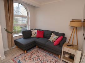 A corner sofa with cushions beside an arched window with curtains a wooden floor lamp and a side table with a remote on a rug at 1 Ilsham Cottages in Torquay