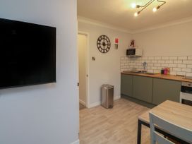 A kitchen area with green cabinets wooden countertops a microwave mounted on the wall a wall clock and a wall-mounted television at 1 Ilsham Cottages in Torquay