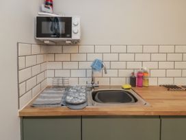 A kitchen sink with a faucet a microwave mounted above and cleaning supplies on the countertop at 1 Ilsham Cottages in Torquay