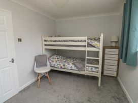 A bedroom with a white bunk bed next to a chest of drawers and a chair with towels at 1 Ilsham Cottages in Torquay