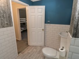 A bathroom with a toilet, sink, white tiled walls, blue painted upper walls, and an open door leading to a room with bunk beds at 1 Ilsham Cottages in Torquay