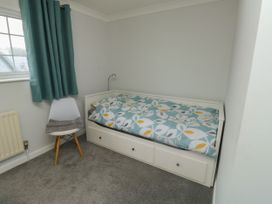 A small bedroom with a single bed with a floral duvet a white chair with a towel near a window with teal curtains at 1 Ilsham Cottages Torquay