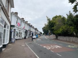 A street with parked cars on the left side and shops on the left with british flags and trees on the right at 1 Ilsham Cottages Torquay
