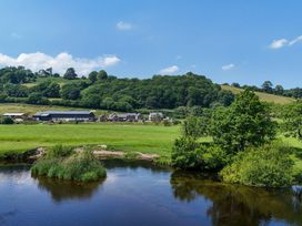 A landscape view with a river, trees, and farm buildings near The Barn in Corwen