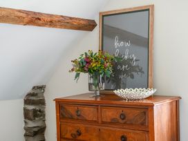 A bedroom with a dresser, flowers in a vase, and framed artwork at The Barn in Corwen