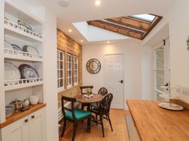 A dining area with a round wooden table and four chairs under a skylight and a wooden countertop with dishware at Two Towers Cottage in Montacute