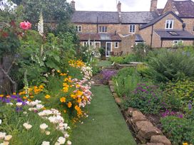 A garden with a grass pathway surrounded by colorful flowers and plants in front of stone houses at Two Towers Cottage in Montacute