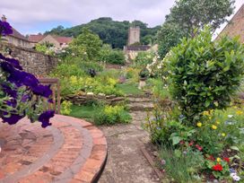 A garden with a stone path shrubs flowers and a round brick table in Montacute