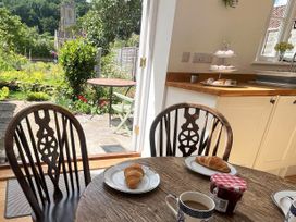A kitchen with a wooden table set with plates holding croissants mugs and a jar of jam with a view of a garden and outdoor table and chairs at Two Towers Cottage in Montacute