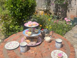 An outdoor round table with a three-tier tray of cupcakes and pastries two mugs a cream jug and a teapot in a garden with flowers at Two Towers Cottage in Montacute