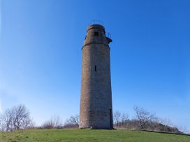 A tall cylindrical stone tower on a grassy hill with leafless trees in the background at Two Towers Cottage in Montacute
