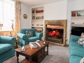 A living room with teal armchairs and sofa a wooden coffee table with a game set built in bookshelves and a fireplace with flowers at Two Towers Cottage in Montacute