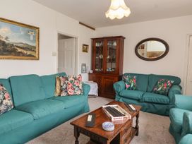 A living room with teal sofas floral cushions a wooden coffee table with board game and plates a wooden cabinet and a wall mirror at Two Towers Cottage in Montacute