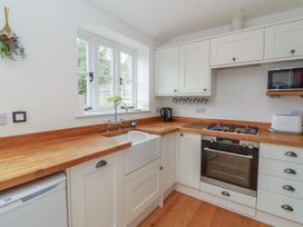 A kitchen with white cabinets wooden countertops a sink a stove an oven a microwave a kettle and a toaster at Two Towers Cottage in Montacute
