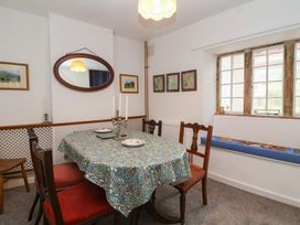 A dining room with a table covered by a patterned cloth surrounded by wooden chairs and a window seat at Two Towers Cottage in Montacute