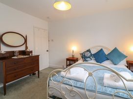 A bedroom with a bed with blue pillows and folded white towels wooden bedside tables with lamps and a wooden dresser with an oval mirror at Two Towers Cottage in Montacute