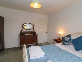 A bedroom with a bed covered by a blue quilt and pillows a wooden dresser with an oval mirror and a nightstand with a lamp at Two Towers Cottage in Montacute