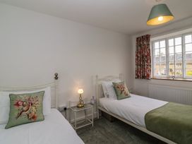 A bedroom with two single beds a bedside table with a lamp and a window with floral curtains at Two Towers Cottage Montacute