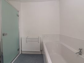 A bathroom with a bathtub a radiator a frosted glass shower door and tiled walls at Two Towers Cottage Montacute