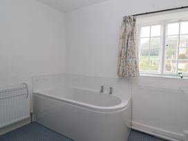 A bathroom with bathtub radiator window and floral curtain at Two Towers Cottage in Montacute