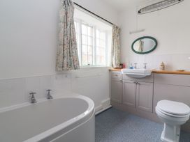 A bathroom with a bathtub toilet sink mirror floral curtains and cupboard at Two Towers Cottage in Montacute