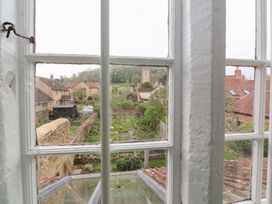 A view of a garden and houses with tiled roofs through a multi-pane window at Two Towers Cottage in Montacute
