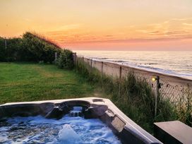 A hot tub near the ocean with a sunset view at Beach Haven Happisburgh, East Anglia