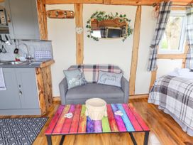 A small living area with a grey sofa, colorful wooden coffee table, kitchenette, and a bed with plaid bedding at Moel Y Parc in Bryniau Clwyd near Denbigh