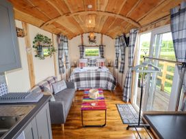 A small wooden room with a bed, grey sofa, colorful table, kitchen sink, window curtains, and sliding glass doors at Moel Y Parc in Bryniau Clwyd near Denbigh