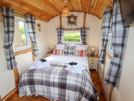 A bedroom with a double bed two bedside tables with lamps windows with plaid curtains and wooden ceiling at Moel Y Parc in Bryniau Clwyd near Denbigh