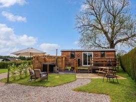 An outdoor area with a wooden cabin surrounded by grass and trees with patio furniture and a hot tub at Moel Y Parc in Bryniau Clwyd near Denbigh