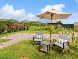 An outdoor seating area with two chairs a small table and a large umbrella on grass with a hedge and plants in the background at Moel Y Parc Bryniau Clwyd near Denbigh