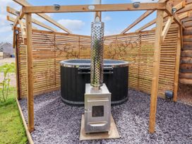 An outdoor hot tub with a wood stove heater under a wooden pergola with slatted fences at Moel Y Parc in Bryniau Clwyd near Denbigh