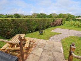 A garden area with a wooden picnic table a paved patio a gravel path and a hedge at Moel Y Parc in Bryniau Clwyd near Denbigh