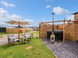 An outdoor seating area with two chairs a small table and an umbrella next to a wooden gazebo with a stove and a hot tub at Moel Y Parc in Bryniau Clwyd near Denbigh
