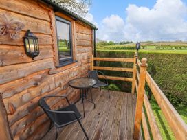 A wooden deck with two black chairs and a glass table overlooking green fields at Moel Y Parc in Bryniau Clwyd near Denbigh