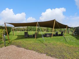 A shaded outdoor seating area with chairs and sofas on grass at Moel Y Parc in Bryniau Clwyd near Denbigh