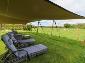 An outdoor seating area with lounge chairs and a small table under a large canopy beside a fenced green field at Moel Y Parc in Bryniau Clwyd near Denbigh