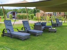 Outdoor patio furniture including lounge chairs, a sofa, and side tables under a canopy on grass at Moel Y Parc in Bryniau Clwyd near Denbigh