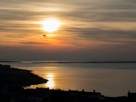 A sunset over a body of water with buildings in the foreground at Mallards Rest, Llandwrog near Bontnewydd, Gwynedd