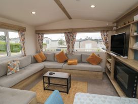 A living room with a gray sectional sofa and orange pillows a coffee table and television at No30 Elm Rise in Gristhorpe near Filey
