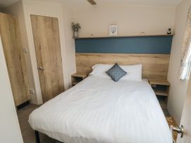 A bedroom with a bed with white linens and a gray pillow a wooden headboard and shelf small plants on the shelf and wooden doors at No30 Elm Rise in Gristhorpe near Filey