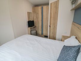 A bedroom with a bed white bedding a wooden wardrobe a small tv on a wooden shelf and a wooden door at No30 Elm Rise Gristhorpe near Filey