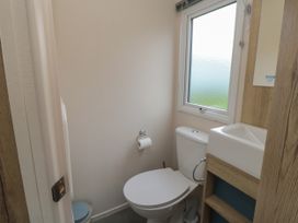 A small bathroom with a toilet a window a sink with a wooden cabinet and a toilet paper holder at No30 Elm Rise in Gristhorpe near Filey
