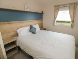 A bedroom with a bed with white linens a wooden headboard and bedside shelves a window with curtains at No30 Elm Rise Gristhorpe near Filey