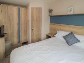 A bedroom with a double bed white bedding a blue cushion wooden wardrobes and a small TV at No30 Elm Rise Gristhorpe near Filey