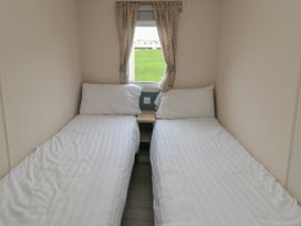 A bedroom with two single beds separated by a small wooden nightstand and a window with patterned curtains at No30 Elm Rise in Gristhorpe near Filey