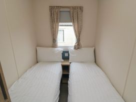 A small bedroom with two single beds separated by a wooden nightstand and a window with patterned curtains at No30 Elm Rise in Gristhorpe near Filey