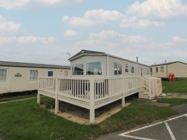 A static caravan with a white railing deck on a grassy area at No30 Elm Rise in Gristhorpe near Filey